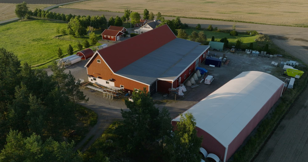 En ladugård och flera hus omringade av fält och gröna träd