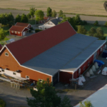 Ladugård och hus sett från ovan bredvid fält.