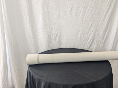 Ett vitt rör på ett bord med svart duk framför en vit hängande duk.