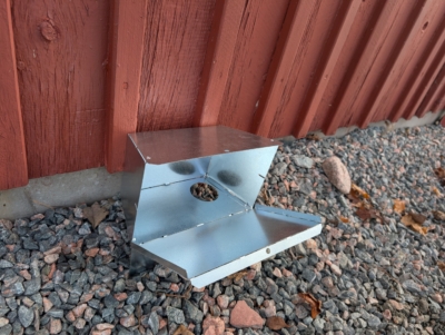 En så kallad Ratbox på grus bredvid en faluröd vägg.